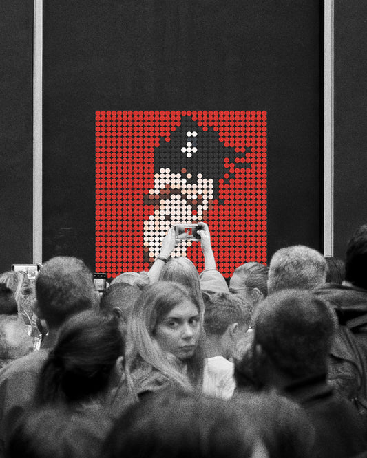 Multitud de personas observan y fotografían una obra de arte en un museo. La obra, enmarcada sobre una pared negra, está compuesta por piezas circulares tipo LEGO que forman una imagen pixelada de la portada del álbum MOTOMAMI + de Rosalía, sobre fondo rojo. La imagen destaca en color mientras que el resto de la escena es en blanco y negro.