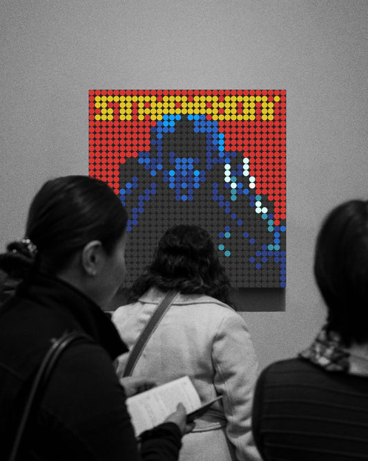 Varias personas observan una obra de arte expuesta en una galería. La pieza, compuesta por fichas circulares tipo LEGO, representa la portada del álbum Starboy de The Weeknd. El retrato del artista aparece en tonos oscuros y azules sobre un fondo rojo intenso, con el título "STARBOY" destacado en letras amarillas en la parte superior. El resto de la imagen está en blanco y negro, haciendo que los colores vibrantes de la obra destaquen aún más en la escena.
