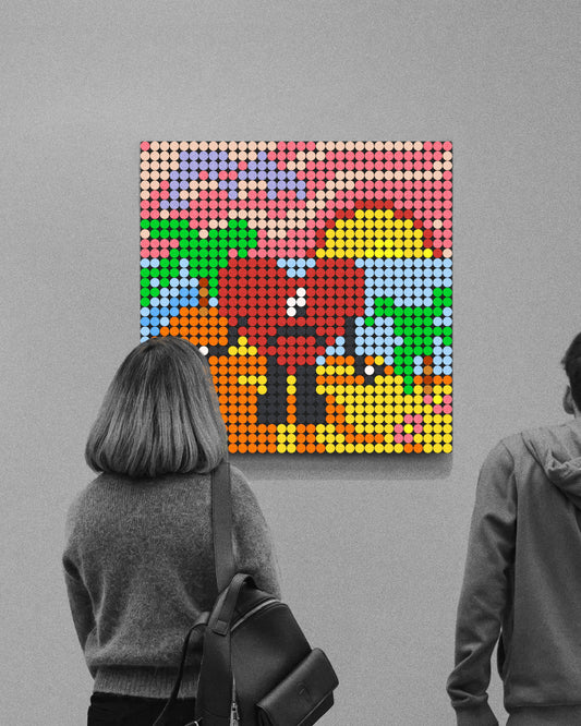 Fotografía en blanco y negro de dos personas observando en una galería un mosaico colorido hecho con piezas circulares que recrea la portada del álbum Un Verano Sin Ti de Bad Bunny: un corazón rojo con ojos negros y boca triste sobre un paisaje playero con arena amarilla y naranja, palmeras verdes, mar azul y un cielo degradado en tonos rosa y lila, con un sol amarillo parcialmente oculto.